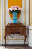 Peonies in blue vase on old bureau against panelled wall