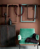 Türkisgrüner Sessel, Holzschrank und Bilderrahmen vor rotbrauner Wand