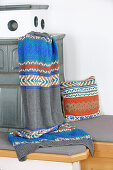 Knitted blanket and cushion with Norwegian pattern on bench of tiled stove