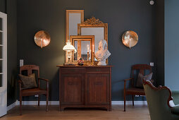 Gilt-framed mirror and bust on antique cabinet against dark wall