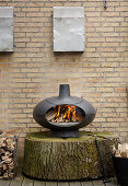 Modern pizza oven on large slice of tree trunk against brick wall