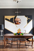 Antique dining table and chairs below copper pendant lamp and modern artwork on wall