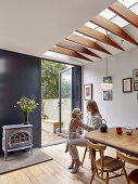Woman and dog at dining table below skylight and next to door leading into garden