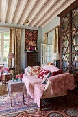 Pink throw on sofa in front of tall, antique bookcase with glass doors