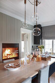 Pendant lamps with spherical glass shades above dining table in front of fire burning in fireplace