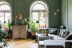 Cabinet, grey sofa set, houseplants and arched window in living room with green walls