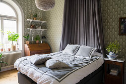 Double bed with canopy in bedroom with patterned wallpaper