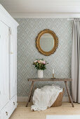 White wardrobe, vase of flowers on rustic bench and gilt-framed mirror in bedroom