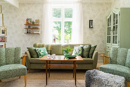 Green upholstered furniture, dresser and patterned wallpaper in living room