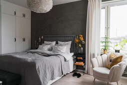 Double bed, white wardrobe and armchair in bedroom with dark grey wall