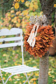 Kranz aus Ahornblättern mit Samenständen von Clematis an Kirschbaum gehängt