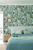 Double bed with blue and green covers in bedroom with botanical wallpaper