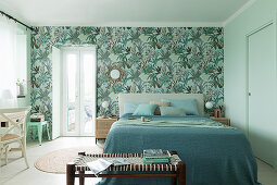 Double bed with blue and green covers and bench in bedroom with botanical wallpaper