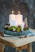 Four white pillar candles, moss and decorations on metal tray