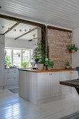 A white kitchen island with a wooden worktop in front of a brick wall