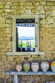 Holzbank mit Tontöpfen vor Steinmauer mit Fensterausschnitt
