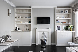 Dummy fireplace and silver urn flanked by floor-to-ceiling shelves and cabinets