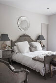 Circular mirror above double bed in room with muted greys and whites