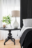 Round, antique bedside table with table lamp and leafy branches