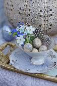 Small Easter decoration with a bouquet of forget-me-nots, cherry blossoms, and Puschkinia in a vase with Easter eggs and feathers
