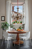 Ornate chandelier above plate of fruit on round antique table and houseplants in background