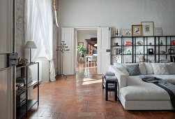 Open shelves and pale sofa in high living room with terracotta floor tiles