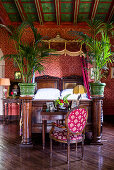 Antique double bed and potted palm trees in bedroom with red wallpaper