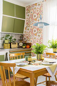 Dining area in front of floral wallpaper in retro kitchen with green fronts