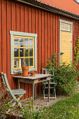 Sitzplatz mit altem Holztisch vorm Schwedenhaus mit gelbem Fenster