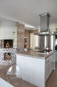Extractor hood above hob on island counter and brick fireplace in open-plan kitchen
