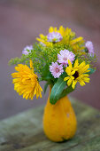 Small bouquet of marigolds, fennel blossoms and daisies in an ornamental pumpkin as a vase