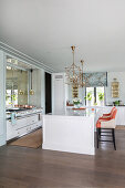 Weißer Mittelblock mit Designerstühlen in eleganter, offener Küche