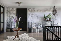 Vase of gladioli on round, antique table on animal-skin rug in elegant foyer with mural wallpaper