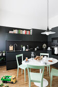 Black fitted kitchen, white table, green chairs and toys on the floor