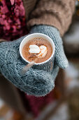 Hände mit Handschuhen halten heiße Schokolade mit Marshmallow