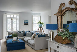 Pale grey sofa with scatter cushions and blue ottoman used as coffee table