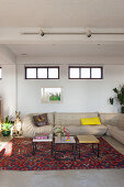 Pale leather couch and set of coffee tables on colourful rug in renovated loft apartment
