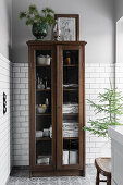 Glass-fronted cabinet in bathroom with white wall tiles and Moroccan floor tiles