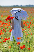 Girl holding bunch of flowers in field of barley and poppies