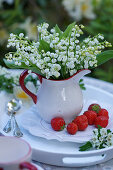 Bouquet of lilies of the valley in creamer pitcher on a plate with strawberries
