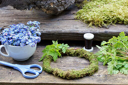 Ingredients for forget-me-not wreath: forget-me-not flowers, cranesbill leaves, moss wreath, scissors, and floral wire