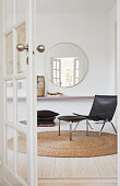 Black leather chair with footstool on round natural carpet, round mirror mounted on a wall