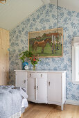 White chest of drawers below picture of horse in bedroom with blue wallpaper