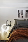 Doppelbett mit grauer Bettwäsche und Überwurf, Beistelltisch und Leuchtobjekt