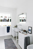 Badezimmer mit weißen Möbeln und Bücherregal vor dem Fenster