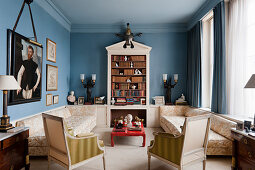 Symmetrical, Wedgewood-blue sitting room with bookcase, sofas, red lacquered coffee table and historical portrait