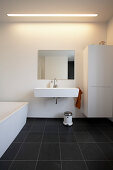 White sink cupboard and bathtub in bathroom with black tiled floor