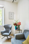 Grauer Sessel, Beistelltisch mit Blumen und Sofa im Wohnzimmer
