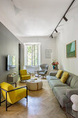Gelbe Sessel, Couchtisch und graues Sofa in schmalem Wohnzimmer