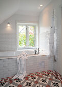 Badewanne im Badezimmer mit weißen Wandfliesen und gemusterten Bodenfliesen